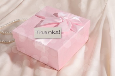 Image of Thanks card and gift box on beige fabric, bokeh effect