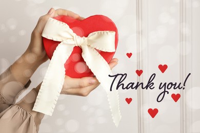 Image of Thank you card design with gift box in woman's hands against white wall. Bokeh effect