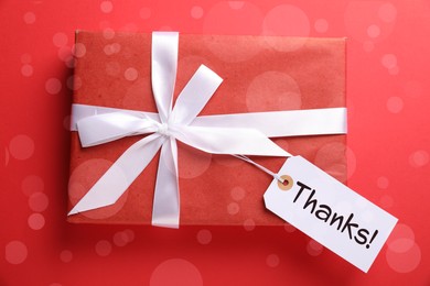 Image of Thanks tag attached to gift box on red background. Bokeh effect