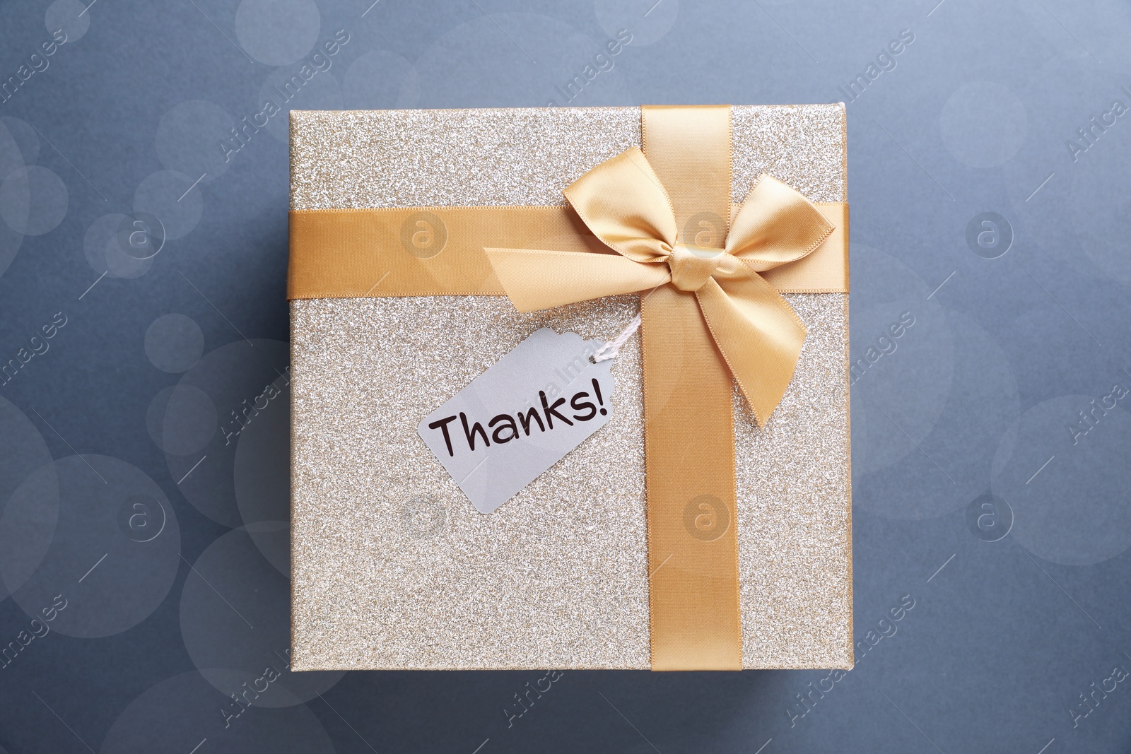 Image of Thanks tag attached to gift box on pale blue background. Bokeh effect