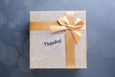 Image of Thanks tag attached to gift box on pale blue background. Bokeh effect
