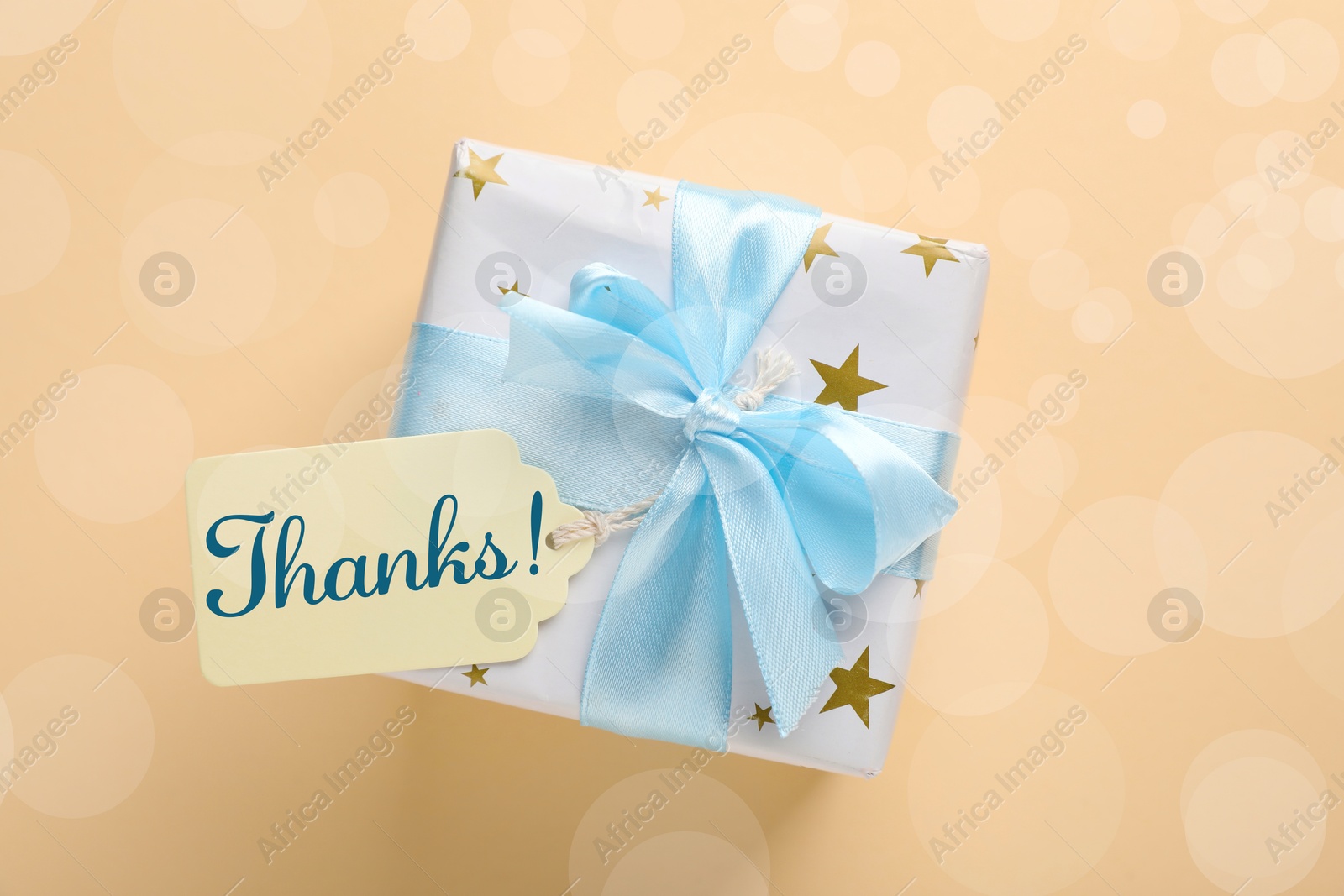 Image of Thanks tag attached to gift box on dark beige background. Bokeh effect