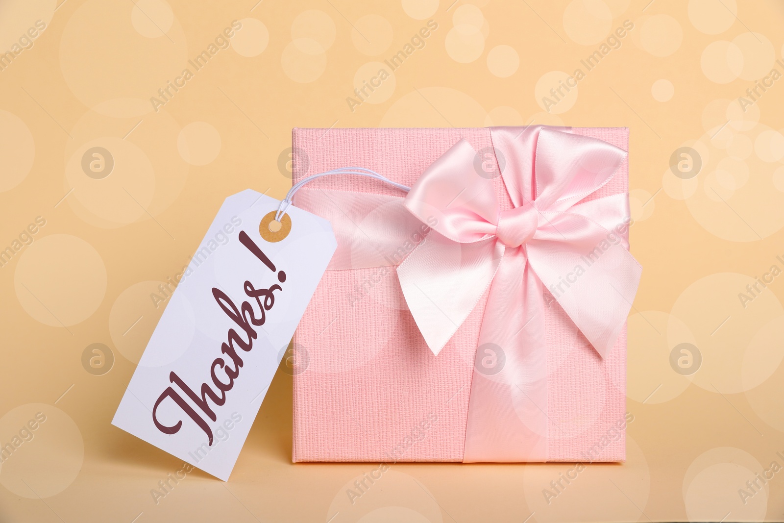 Image of Thanks tag attached to gift box on dark beige background. Bokeh effect