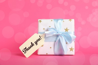 Image of Thanks tag attached to gift box on pink background. Bokeh effect