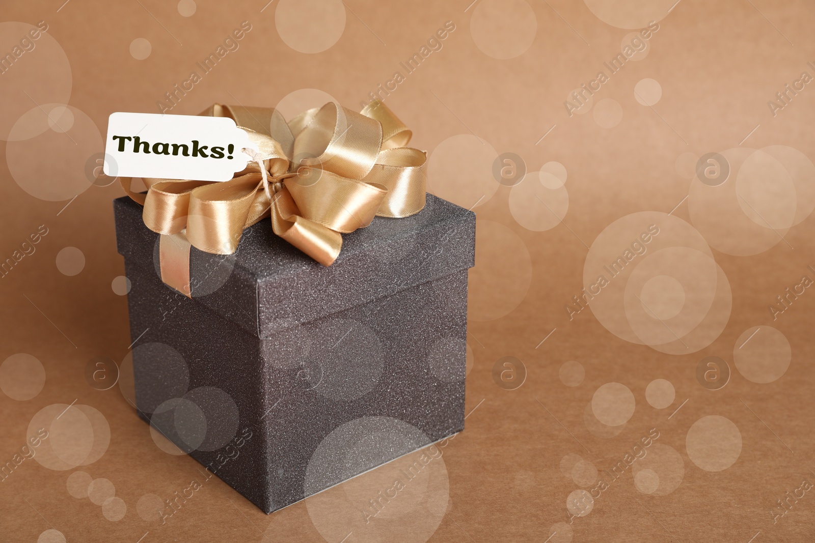 Image of Thanks tag attached to gift box on pale brown background. Bokeh effect