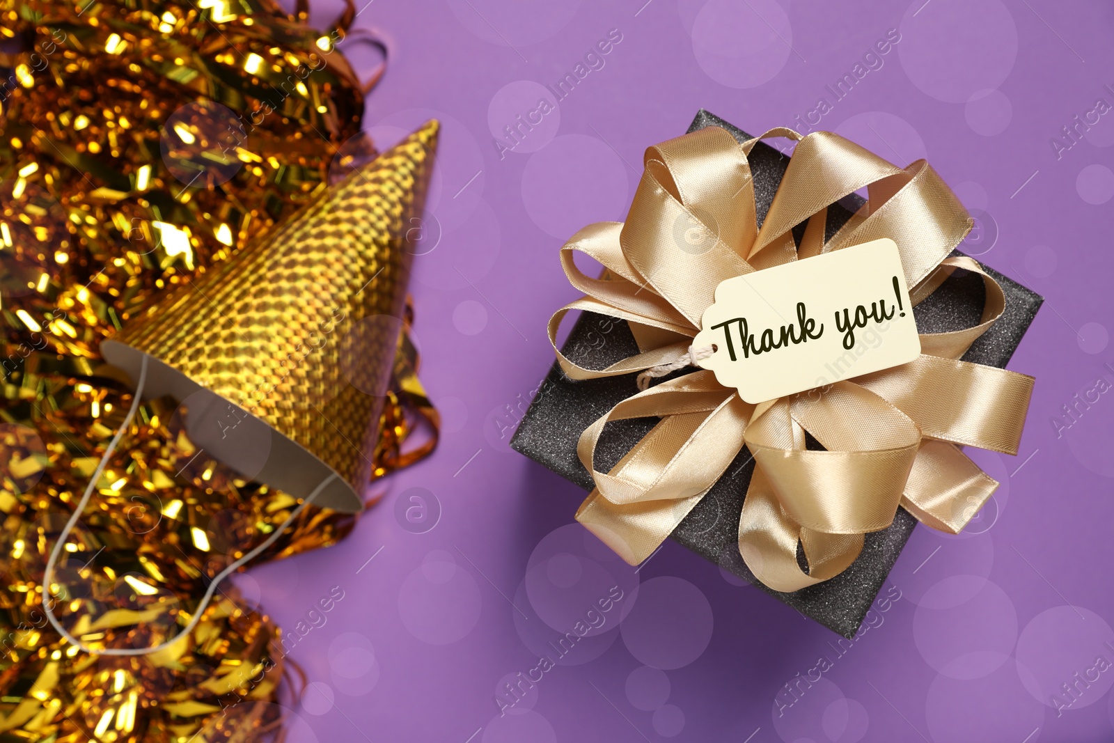 Thanks tag attached to gift box, shiny confetti and party cap on violet background. Bokeh effect Image of Thanks tag attached to gift box, shiny confetti and party cap on violet background. Bokeh effect