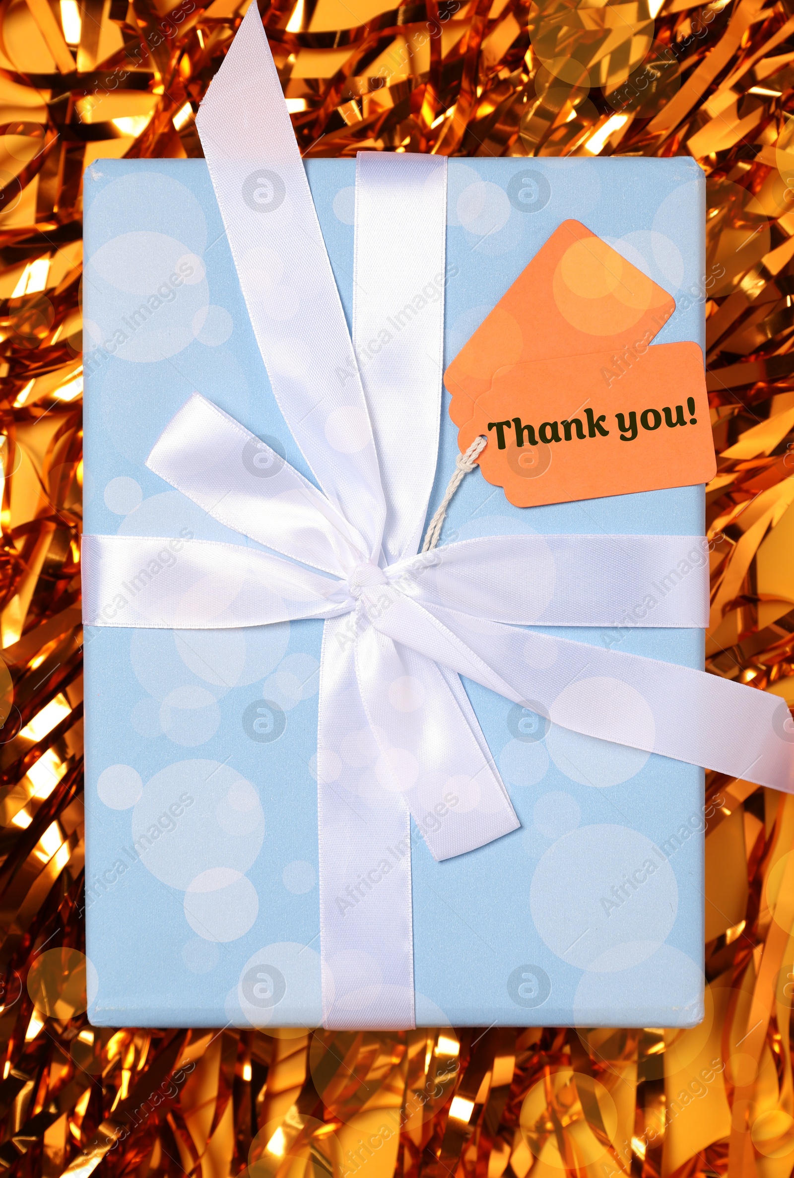 Image of Thanks tag attached to gift box on shiny orange confetti. Bokeh effect