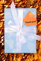 Image of Thanks tag attached to gift box on shiny orange confetti. Bokeh effect