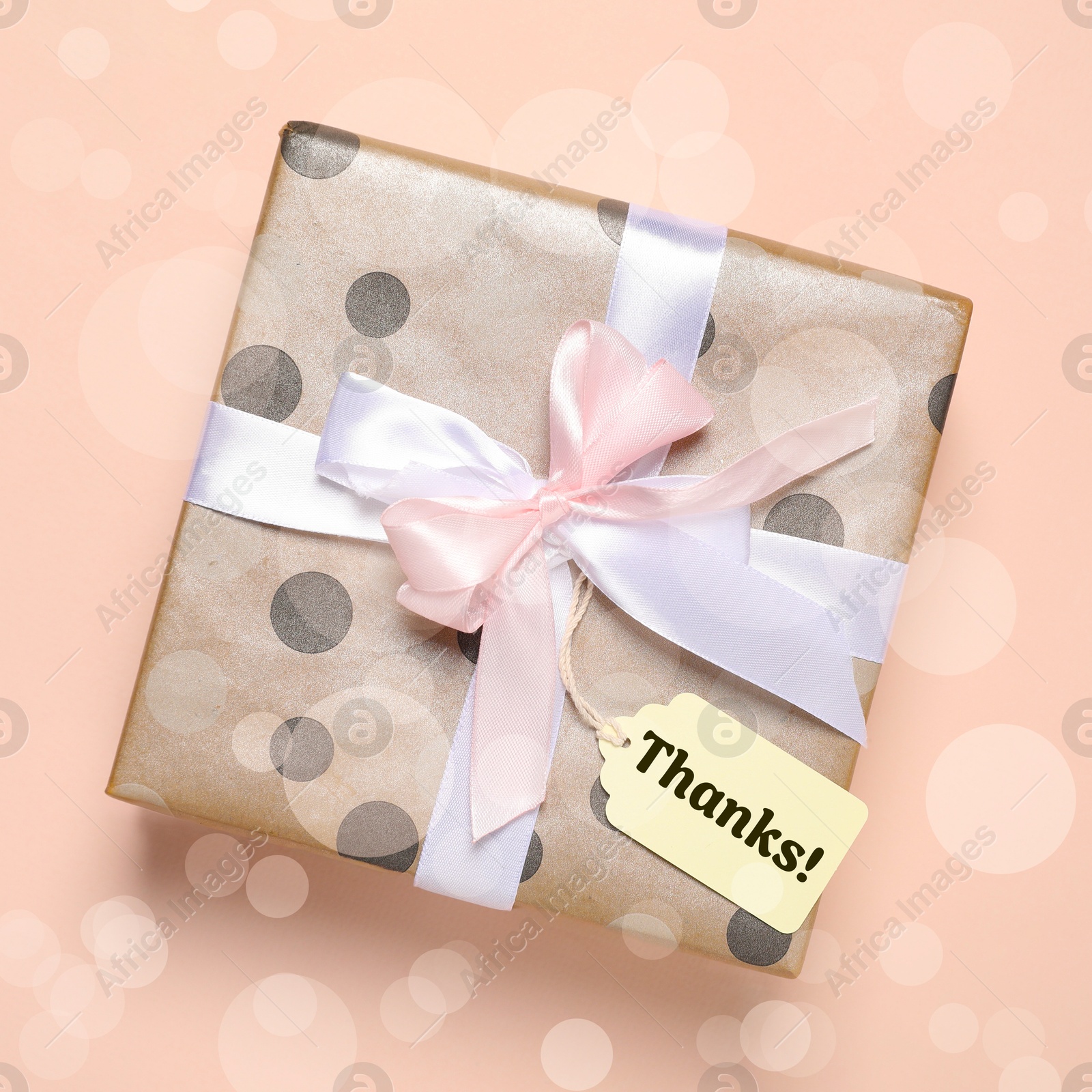 Image of Thanks tag attached to gift box on dark beige background. Bokeh effect