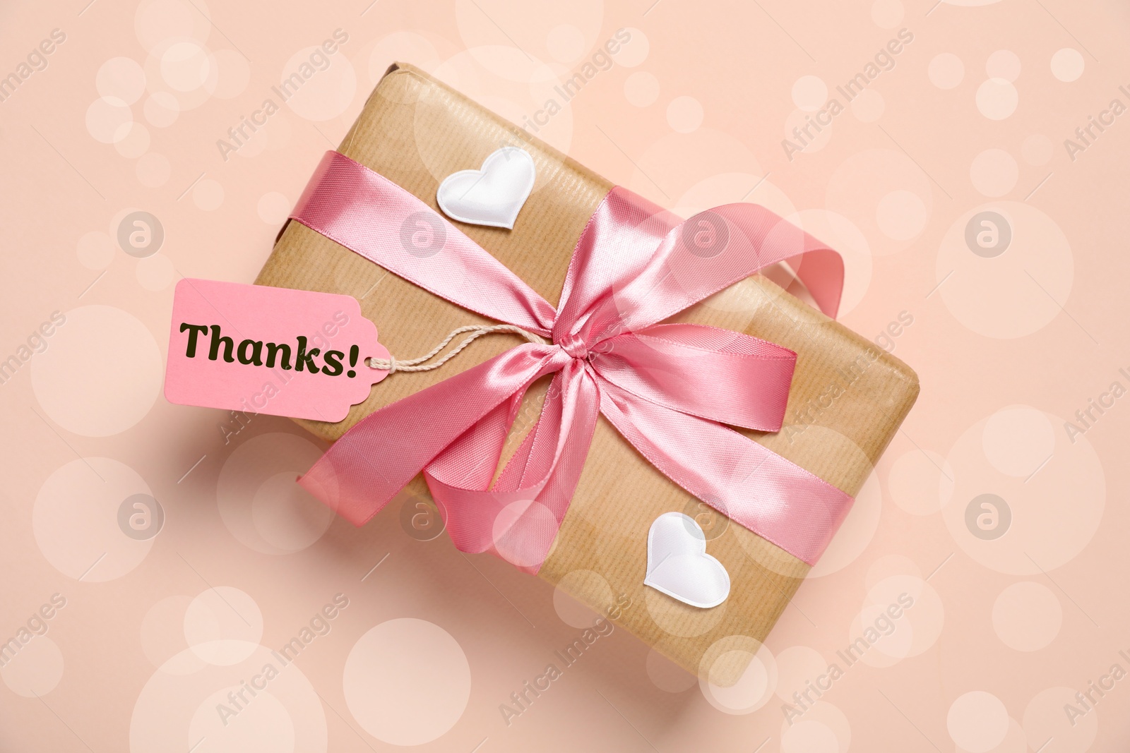 Image of Thanks tag attached to gift box on dark beige background. Bokeh effect