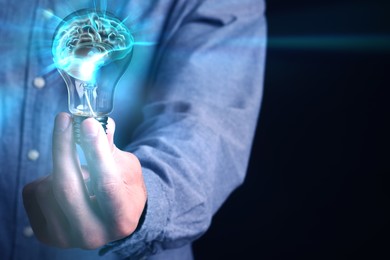 Image of Man holding light bulb with brain illustration inside against black background, closeup. Idea concept