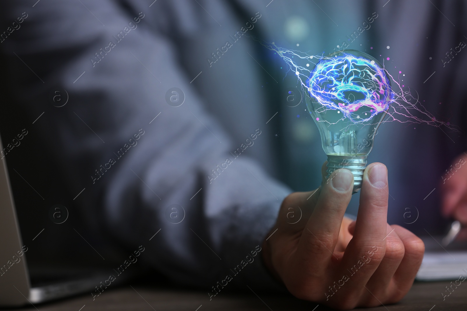 Image of Man holding light bulb with brain illustration inside at table, closeup. Idea concept