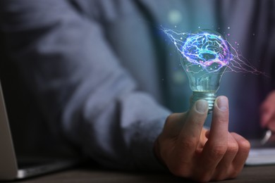 Image of Man holding light bulb with brain illustration inside at table, closeup. Idea concept