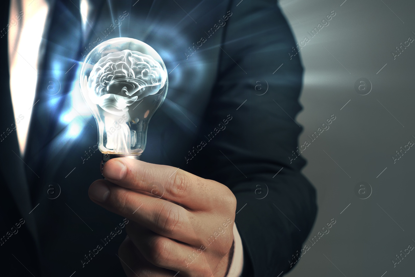 Image of Businessman holding light bulb with brain illustration inside against grey background, closeup. Idea concept