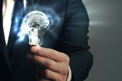 Image of Businessman holding light bulb with brain illustration inside against grey background, closeup. Idea concept