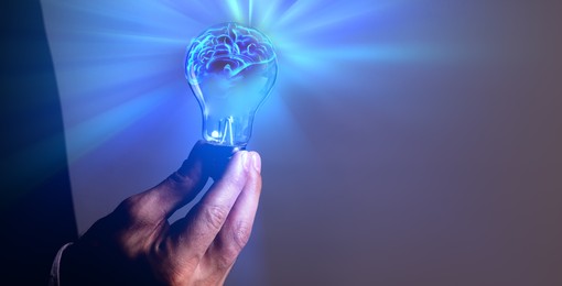 Image of Businessman holding light bulb with brain illustration inside against dark background, closeup. Idea concept