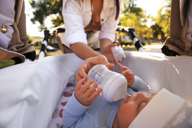 Photo of Young mother feeding her baby during walk in park, view from stroller