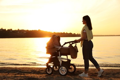Photo of Happy mother with baby in stroller walking near river at sunset