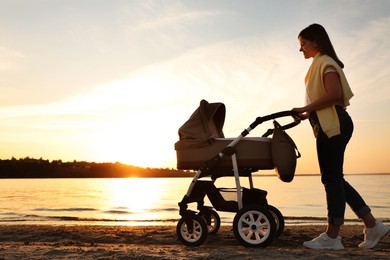 Photo of Happy mother with baby in stroller walking near river at sunset