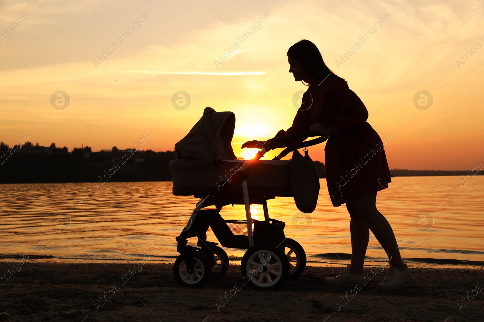 Photo of Happy mother with baby in stroller near river at sunset