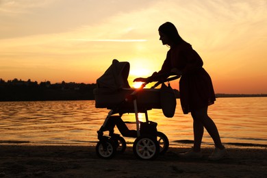 Photo of Happy mother with baby in stroller near river at sunset