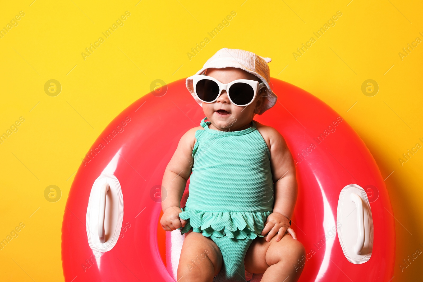 Photo of Cute little baby in sunglasses with inflatable ring on yellow background