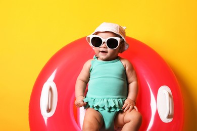 Photo of Cute little baby in sunglasses with inflatable ring on yellow background