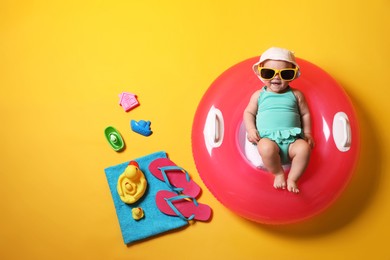Photo of Cute little baby in sunglasses with inflatable ring and beach accessories on yellow background, top view