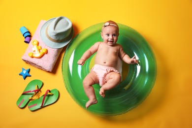 Photo of Cute little baby with inflatable ring and beach accessories on yellow background, top view