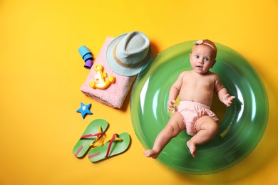 Photo of Cute little baby with inflatable ring and beach accessories on yellow background, top view