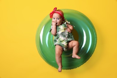 Photo of Cute little baby in headband with inflatable ring on yellow background