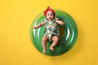 Photo of Cute little baby in headband with inflatable ring on yellow background