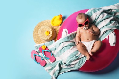 Photo of Cute little baby in sunglasses with inflatable ring and beach accessories on light blue background, top view