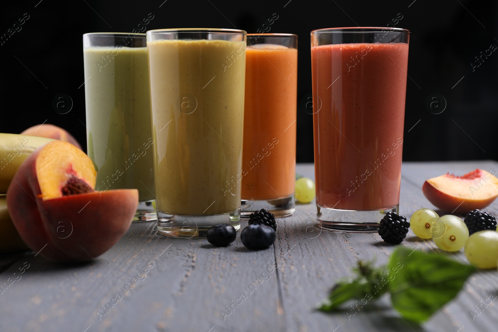 Photo of Many different delicious smoothies and ingredients on grey wooden table against dark background