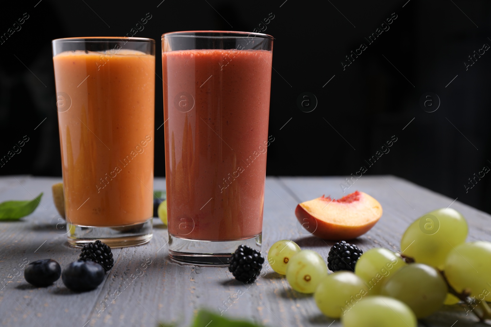 Photo of Different delicious smoothies and ingredients on grey wooden table against dark background