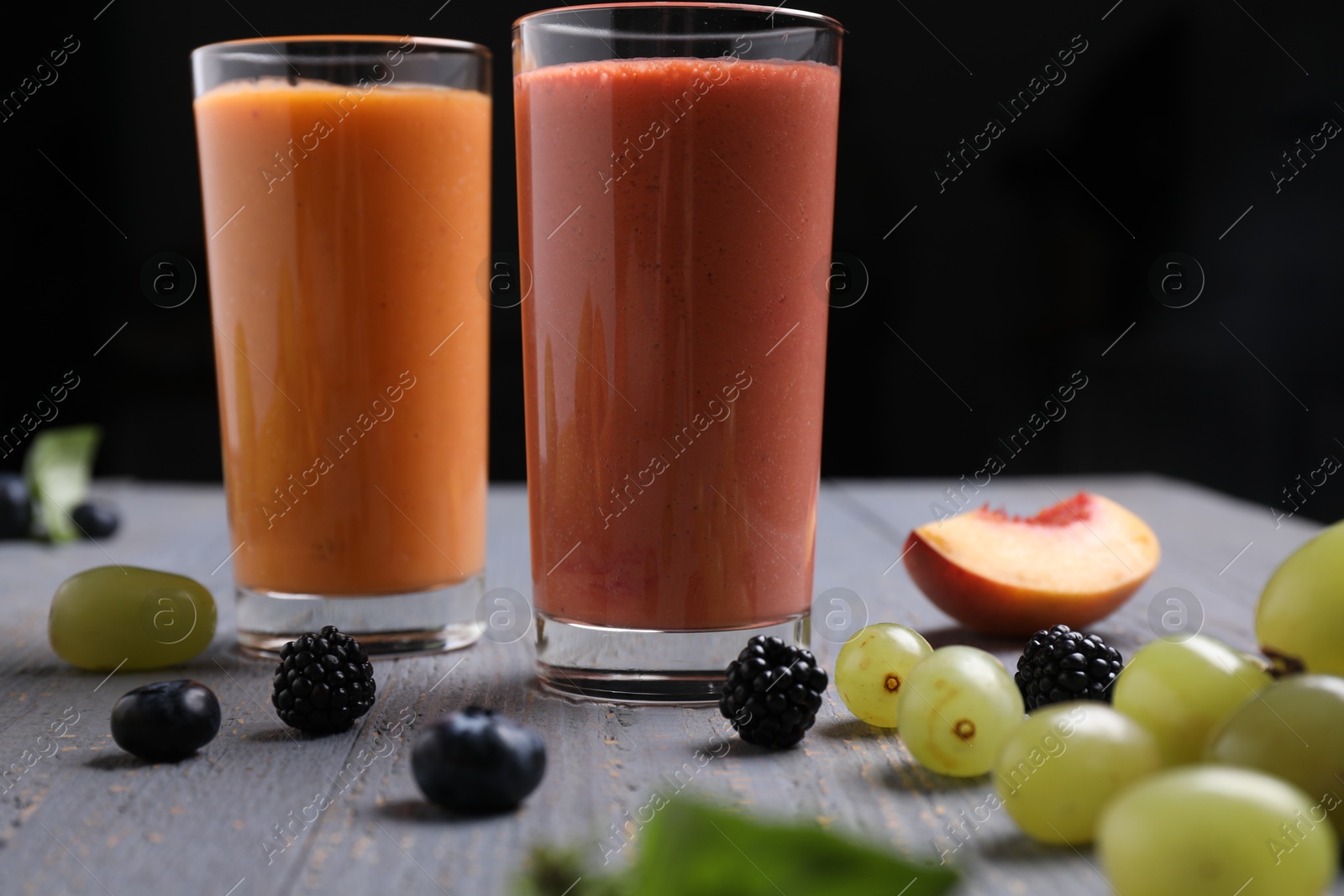 Photo of Different delicious smoothies and ingredients on grey wooden table against dark background