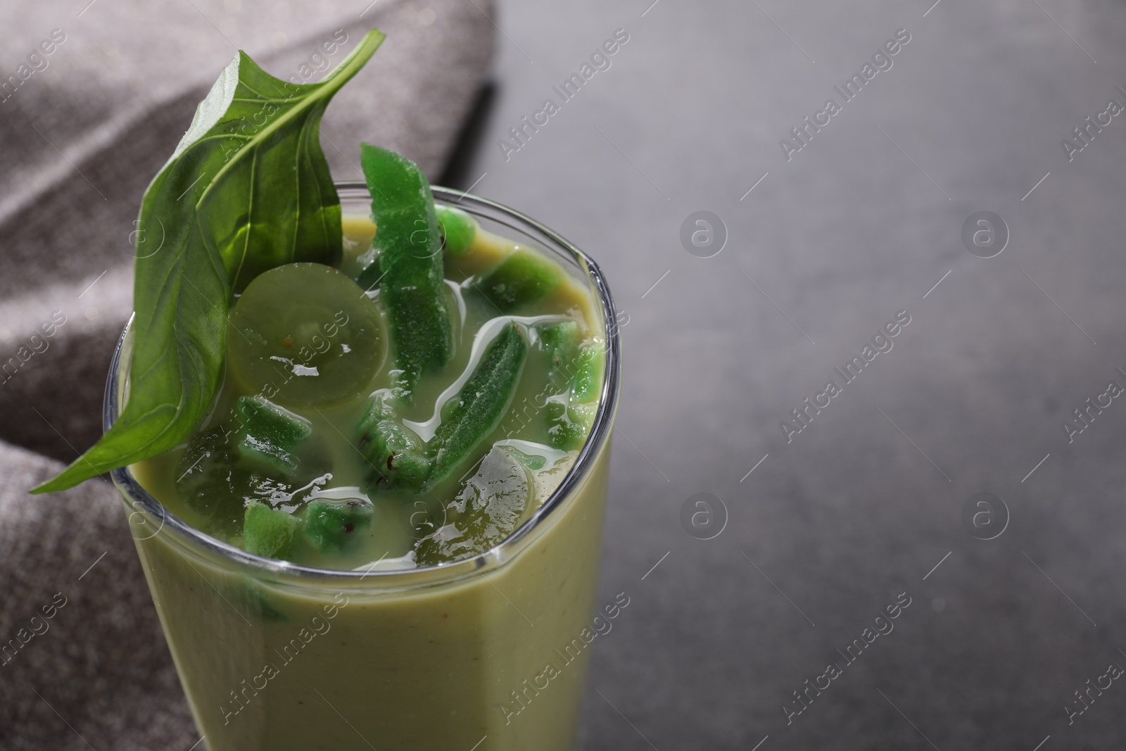 Photo of Glass of delicious smoothie with grape, candied kiwi and basil on grey table, closeup. Space for text