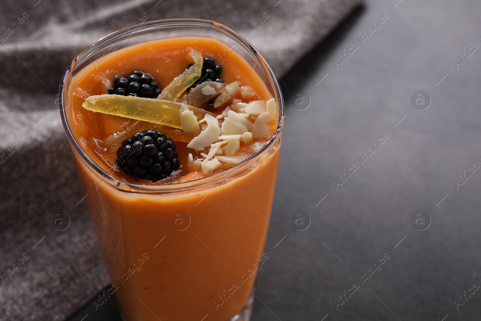 Photo of Glass of delicious smoothie with blackberries, candied mango and almond on grey table, closeup. Space for text