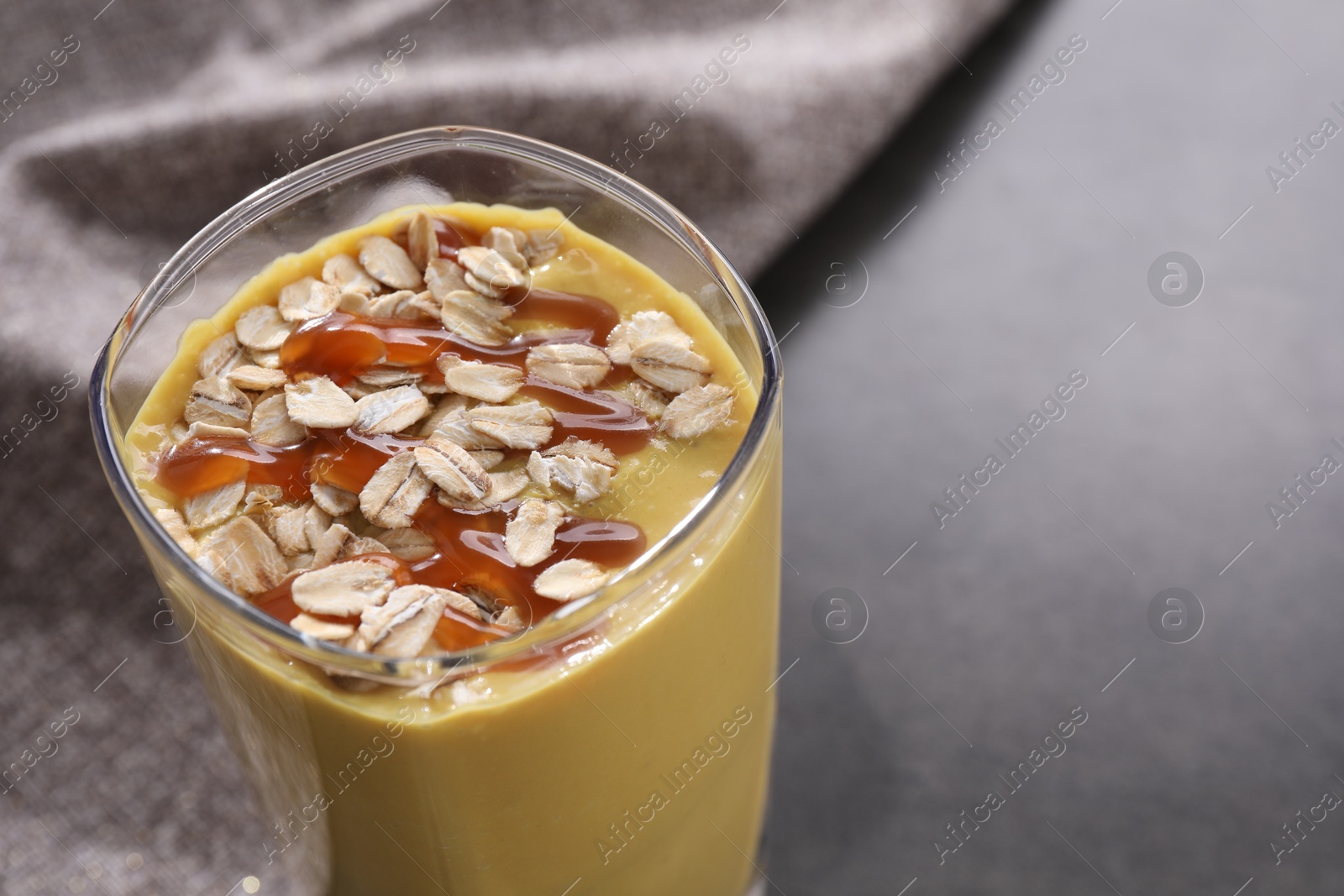 Photo of Glass of delicious smoothie with oat flakes and caramel syrup on grey table, closeup. Space for text