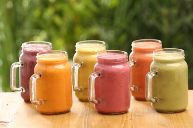 Photo of Many different delicious smoothies in mason jars on wooden table against blurred background