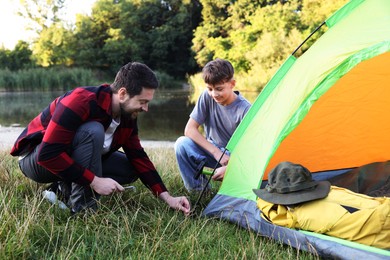 Photo of Father and son setting up camping tent near river outdoors
