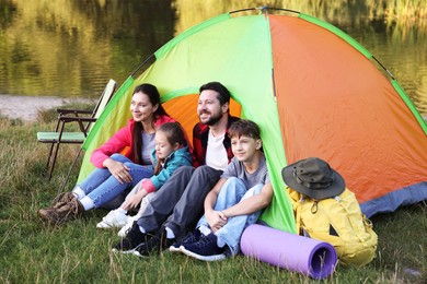 Photo of Happy family spending time together with camping tent and tourist equipment near river outdoors