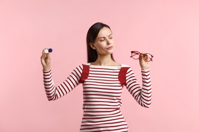Photo of Woman choosing between glasses and contact lenses on pink background