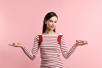 Photo of Woman choosing between glasses and contact lenses on pink background