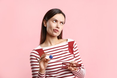 Photo of Woman choosing between glasses and contact lenses on pink background