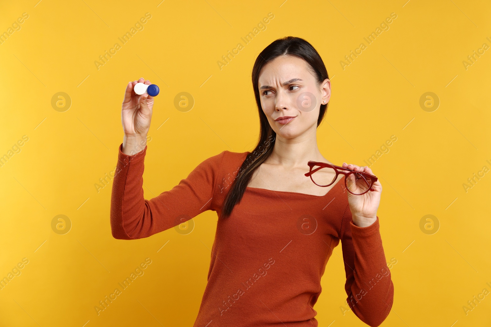 Photo of Woman choosing between glasses and contact lenses on orange background