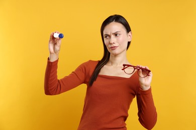 Photo of Woman choosing between glasses and contact lenses on orange background