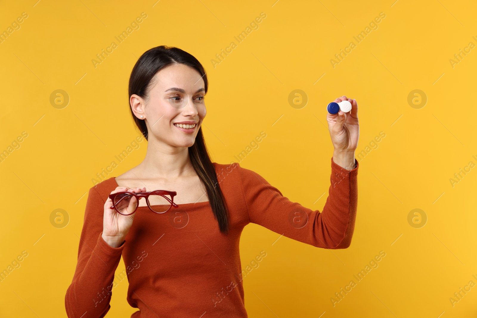 Photo of Woman choosing between glasses and contact lenses on orange background