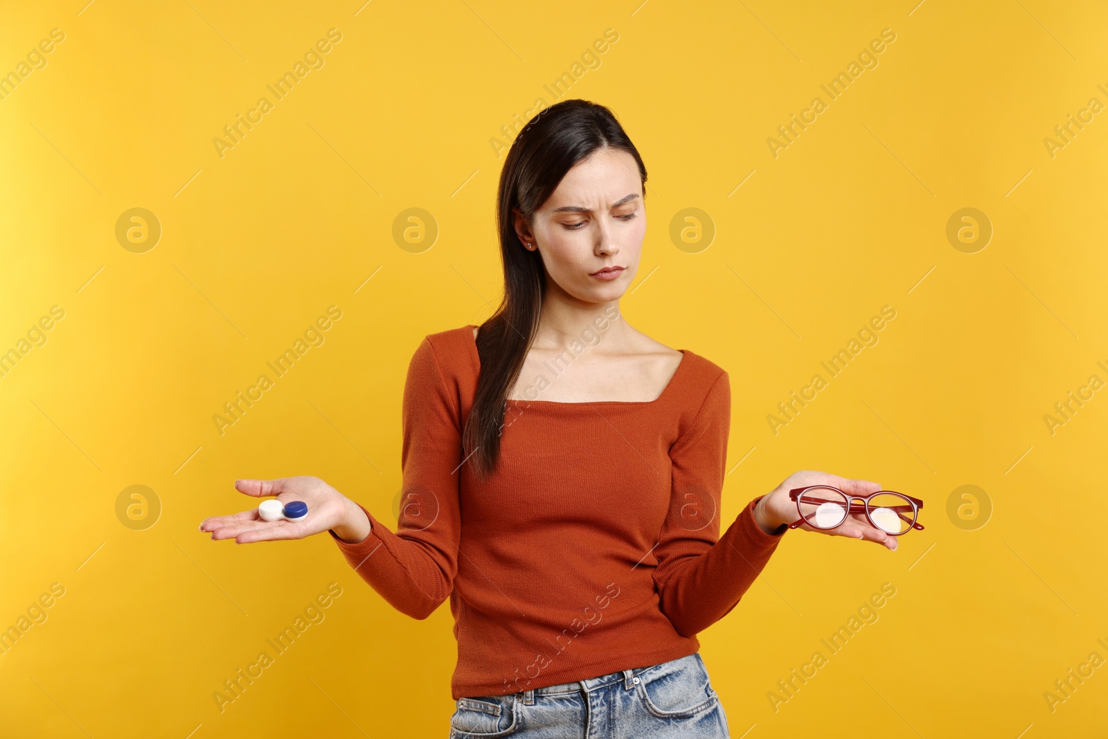 Photo of Woman choosing between glasses and contact lenses on orange background