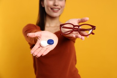 Photo of Woman choosing between glasses and contact lenses on orange background, selective focus